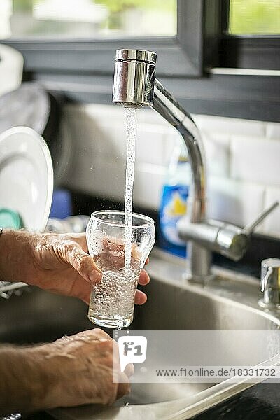 Mann gießt in der Küche Wasser in ein Glas  Nahaufnahme