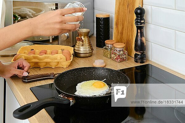 Closeup view of female hand seasoning scrambled eggs with salt on a pan