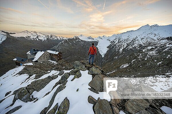 Hiker looking at mountain panorama and glacier  mountain hut Ramolhaus in autumn with snow  at sunset  view of Gurgler Ferner with summit Hochwilde and Falschungsspitze  Ötztal Alps  Tyrol  Austria  Europe