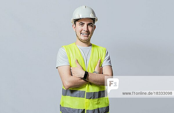 Porträt eines lächelnden  gut aussehenden Ingenieurs auf weißem Hintergrund  Porträt eines jungen Ingenieurs mit Helm und Weste  isoliert. Junge lächelnde Ingenieur trägt Helm und Weste mit verschränkten Armen isoliert