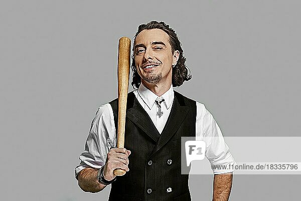 Dramatischer Mann in weißem Hemd und schwarzer Weste mit langen lockigen Haaren hält Baseballschläger