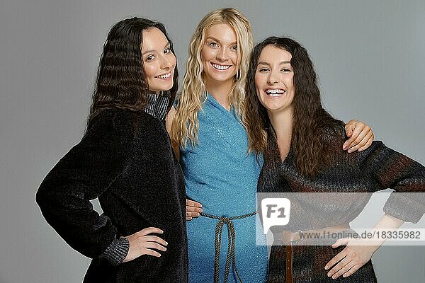 Drei attraktive Mädchen in Wollmänteln posieren im Studio. Glücklich lächelnde Freundinnen. Natürliches Make-up