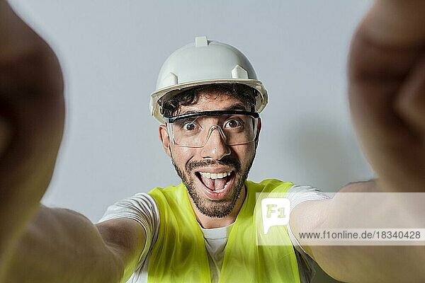 Lächelnder männlicher Ingenieur  der ein Selfie macht und in die Kamera schaut. Funny builder engineer taking a selfie isolated  Engineer taking a selfie isolated. Blick auf männliche Ingenieur  der ein Selfie isoliert