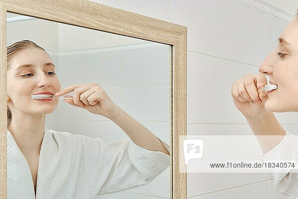 Young woman brushes her teeth in front of the mirror in bathroom in the morning