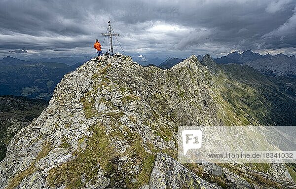 Wanderer auf dem Gipfel der Raudenspitze mit Gipfelkreuz  schmaler felsiger Bergkamm  dramatischer Wolkenhimmel  Karnischer Alpen  Kärnten  Österreich  Europa