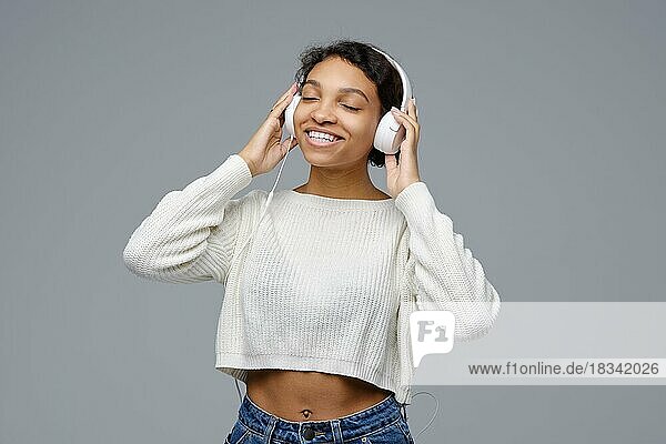Lächelnde afrikanisch-amerikanische Frau  die mit Kopfhörern vor grauem Hintergrund Musik hört