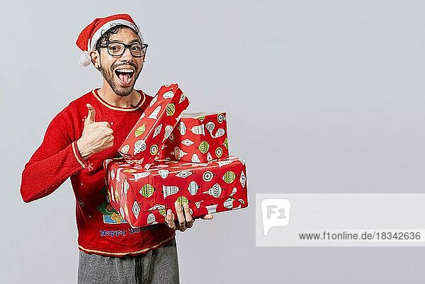 Lächelnder Mann in Weihnachtsmütze hält Weihnachtsgeschenkboxen und gibt Daumen hoch. Freundlicher Mann in Weihnachtskleidung hält Geschenkboxen  Weihnachtsmann hält Geschenkboxen und lächelt mit Daumen nach oben