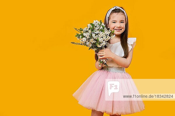 Fröhliches kleines Kind mit Frühlingsblumen in den Händen auf leuchtend gelbem Hintergrund