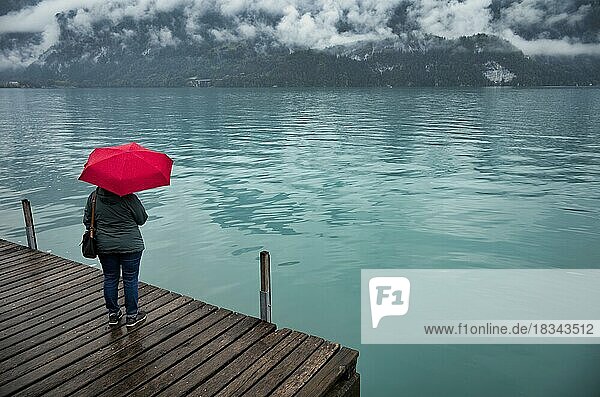 Ältere Frau  Best-Ager  mit rotem Regenschirm  schlechtes Wetter  Seepromenade am Brienzersee  Brienz  Kanton Bern  Berner Oberland  Schweiz  Europa