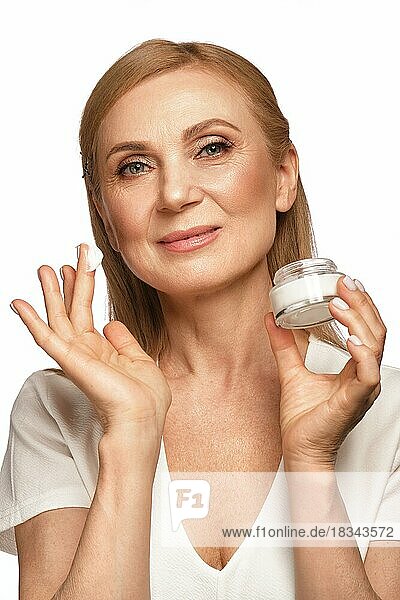 Portrait of a beautiful elderly woman in a white shirt with a moisturizing face cream in her hands