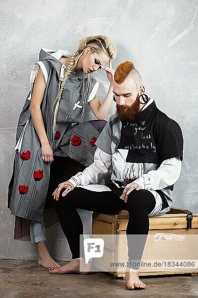 Kreatives ungewöhnliches blondes Mädchen und rothaariger Mann in Designerkleidung und mit Zöpfen auf dem Kopf posieren im Studio