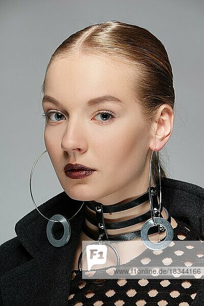 Headshot of a rebel girl with leather collar  metal earrings  smooth hair and dark brown lipstick