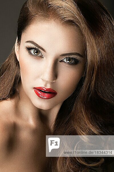 Schöne Frau mit Abend-Make-up  roten Lippen und Locken. Schönes Gesicht. Bild im Studio auf einem grauen Hintergrund genommen