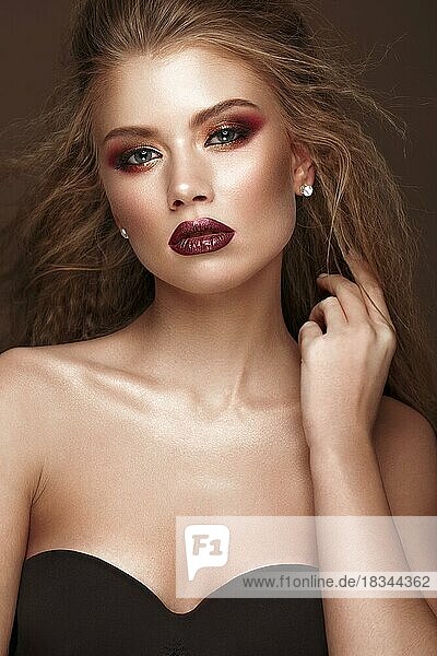 Schöne blonde Modell mit Locken  hellen Make-up und roten Lippen. Die Schönheit des Gesichts. Porträtaufnahme im Studio auf einem braunen Hintergrund