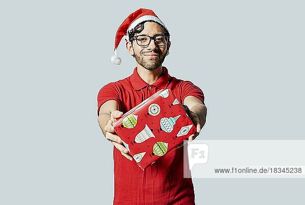 Lächelnder Mann mit Weihnachtsmütze bietet Ihnen eine Weihnachtsgeschenkbox an. Weihnachten Mann bietet ein Geschenk-Boxen isoliert. Handsome Mann in Weihnachten Kleidung zeigt ein Geschenk-Box