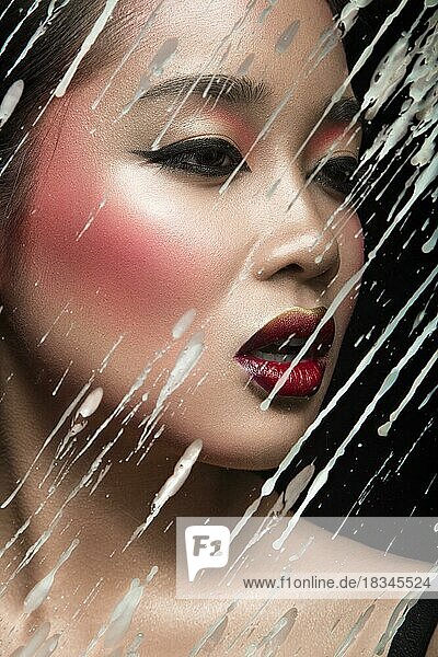 Schöne asiatische Mädchen mit hellen Make-up hinter Glas mit Tropfen von Wachs. Schönes Gesicht. Bild im Studio auf einem schwarzen Hintergrund genommen