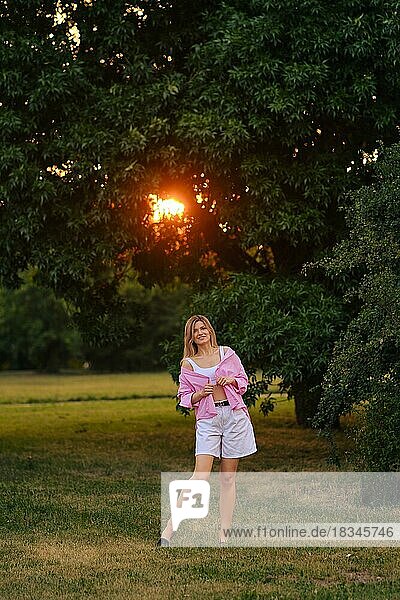Positive Frau in rosa Shirt und weißen Shorts im Park bei Sonnenuntergang
