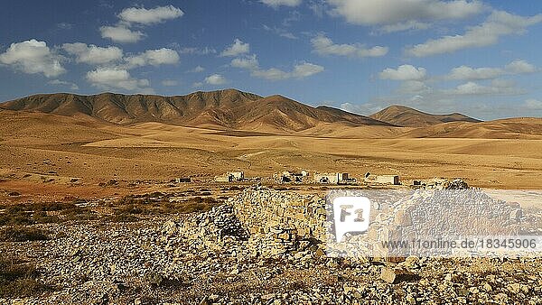 Inselinneres  karge Landschaft  rotbraune Hügel  Gebäuderuinen weiter entfernt  Ruine im Vordergrund  blauer Himmel  weiße Wolken  Fuerteventura  Kanarische Inseln  Spanien  Europa