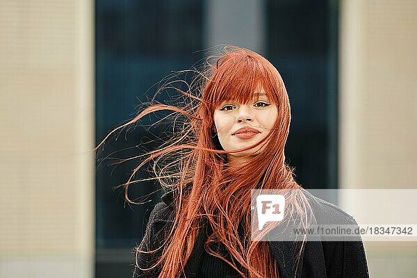 Straßenporträt einer glücklichen jungen rothaarigen Frau an einem windigen Tag