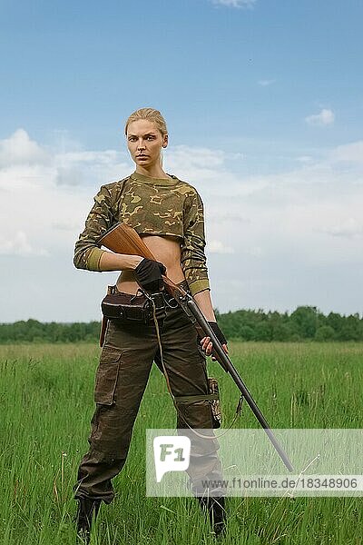 Attraktives Jägermädchen mit doppelläufigem Jagdgewehr steht in der Mitte des Feldes