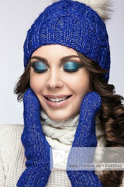 Schönes Mädchen mit sanftem Make-up  Locken und einem Lächeln in winterlicher blauer Strickmütze. Warmes Winterbild. Schönes Gesicht. Bild im Studio aufgenommen
