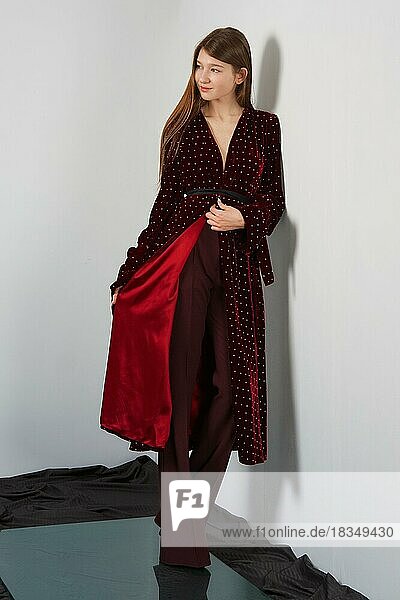 Attractive fashion model in pants and long robe posing for look book near gray wall