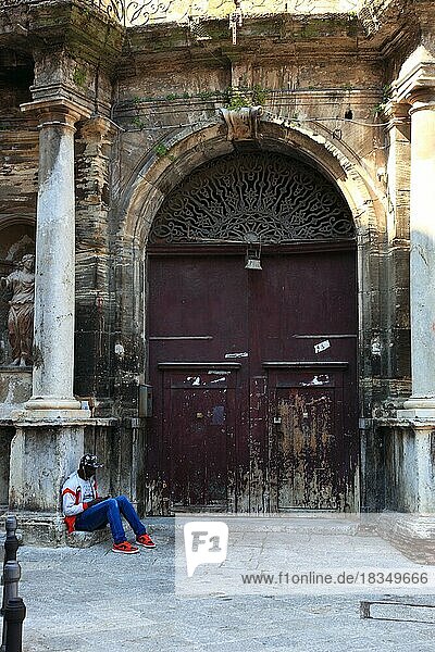Palermo  main entrance of a morbid house at the square Piazza Bologna in the old town  in front of it sits a young African with a mobile phone  Sicily  Italy  Europe