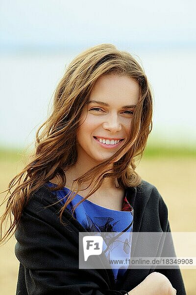 Smiling pretty girl on a beach on windy day with wool wrap over her shoulders