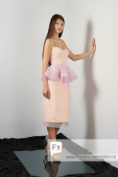 Attraktive Mode-Modell in festlichen Kleid mit Spitze Baske posiert für Lookbook in der Nähe von grauen Wand