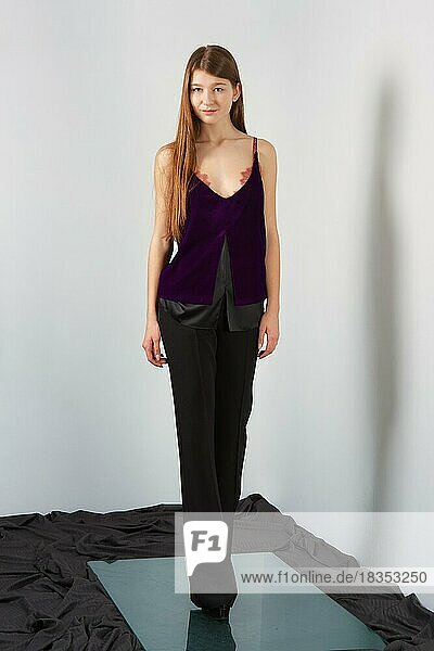 Attraktive Mode-Modell in Hosen und Bluse auf Riemen posiert für Lookbook in der Nähe von grauen Wand