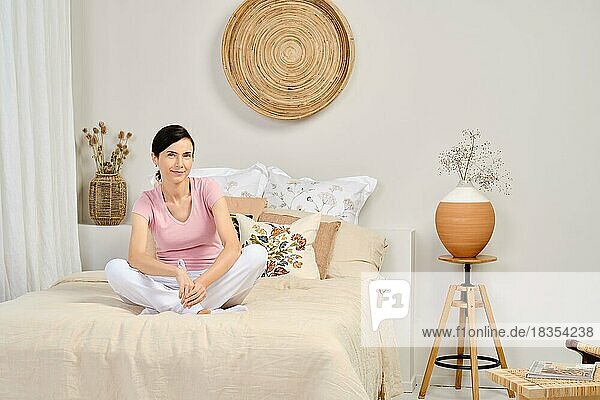 Porträt einer hübschen Frau in Freizeitkleidung  die zu Hause auf dem Bett sitzt