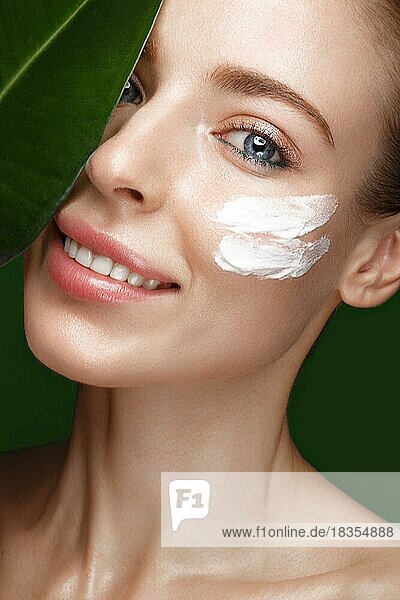 Schönes frisches Mädchen mit Kosmetikcreme auf dem Gesicht  natürliches Make-up und grüne Blätter. Schönes Gesicht. Foto im Studio aufgenommen