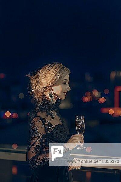 SONY DSCSchönes Mädchen mit einem Glas Champagner in der Nähe des Fensters stehend mit unscharfen Nacht Stadt auf Hintergrund