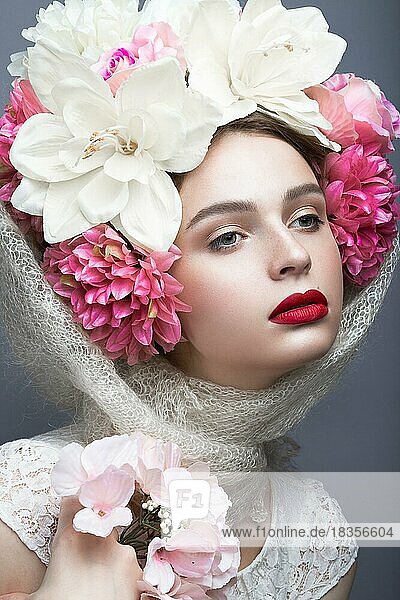Schönes Mädchen mit einem Kopftuch im russischen Stil  mit großen Blumen auf dem Kopf und roten Lippen. Schönheit Gesicht. Bild im Studio auf einem grauen Hintergrund genommen
