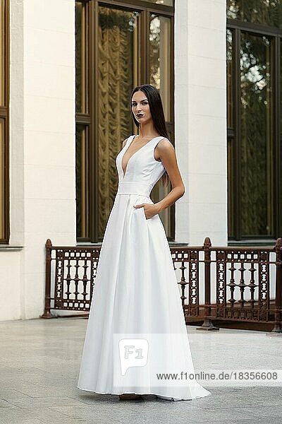 Schönes Mädchen in langem weißen Kleid mit tiefem Ausschnitt. Fashion Model posiert auf der Terrasse eines Palastes