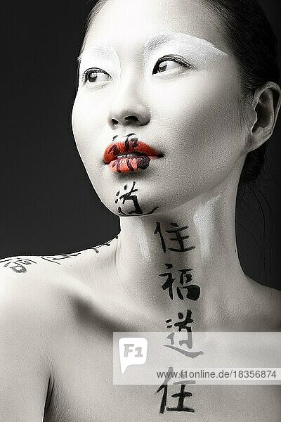 Schönes asiatisches Mädchen mit weißer Haut  roten Lippen und Hieroglyphen im Gesicht. Art Beauty Bild. Bild im Studio auf einem schwarzen Hintergrund aufgenommen