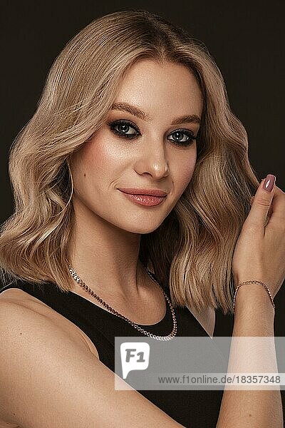 Beautiful blond girl with a perfectly curls hair  and classic make-up. Beauty face and hair. Picture taken in the studio