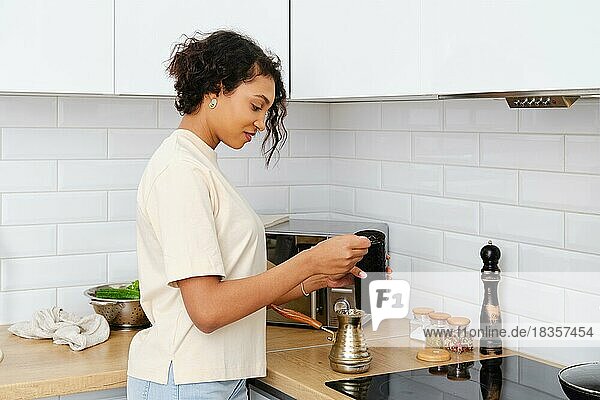 Sleepy african american woman making ground coffee at home in turkish cezve