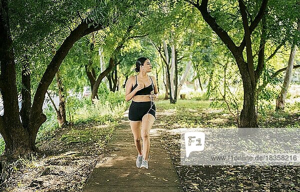 Healthy lifestyle concept of a woman jogging in a green park  Sporty young woman running in a park. Girl running in a park while listening to music  Lifestyle of sporty woman running in a park