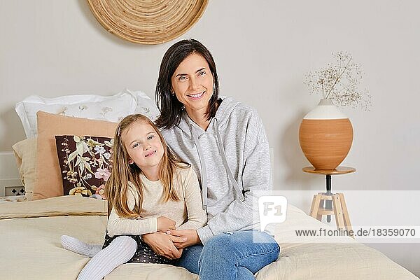 Lifestyle-Foto von Mutter und Tochter  die zu Hause auf dem Bett sitzen