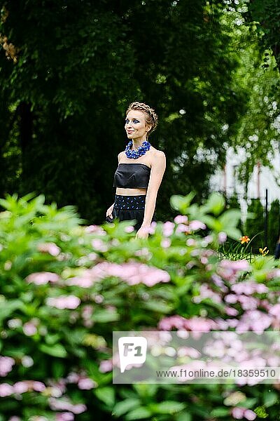 Portrait of cute girl in small topic blouse and breeches walking behind the flower bed