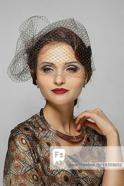 Beautiful fashion model with red mat lips and veil over eyes in silk dress. Clean fresh face of pretty girl with natural makeup