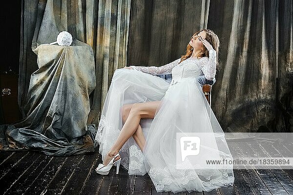 Porträt der hübschen Braut im Hochzeitskleid in voller Länge im Sessel sitzend