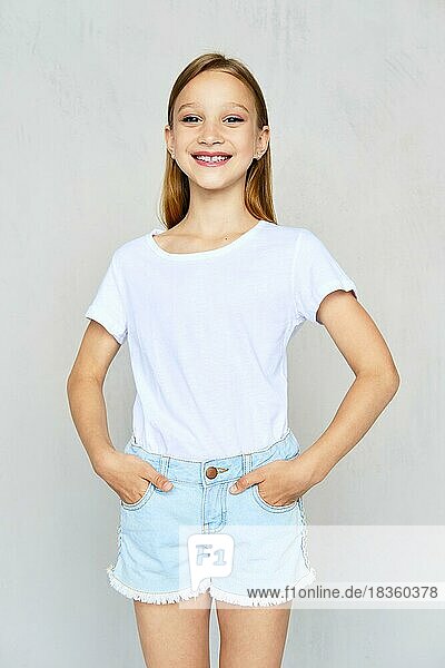 Young sportive girl in white t-shirt with hands in poskets of jeans shorts posing in studio