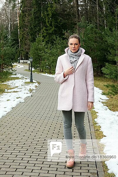 Pretty girl in pink coat walking along pathway in forest