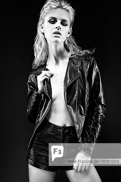 Gewagtes Mädchenmodell in schwarzem Lederkleid im Stil eines Rocks auf einem nackten Körper  dunklem Make-up und nassen Haaren. Das Bild wurde im Studio aufgenommen. Schwarz-Weiß-Bild