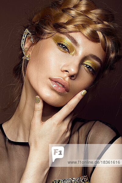 Schönes Mädchen in einem goldenen Kleid mit kreativem Make-up und Zöpfen auf dem Kopf. Die Schönheit des Gesichts. Fotos im Studio geschossen