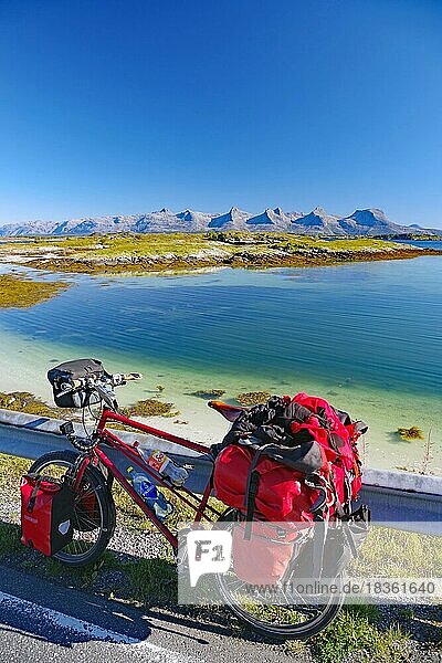 Bepacktes Reiserad  glasklares Wasser in einer seichten Bucht  Sicht auf das Bergmassiv Sieben Schwestern  Fahrradtourismus  Fahrradreise  Insel Heröy FV 17  Kystriksveien  Nordland  Norwegen  Europa