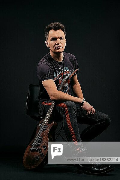 Low-Key-Porträt eines Musikers  der mit einer E-Gitarre auf einem Stuhl sitzt
