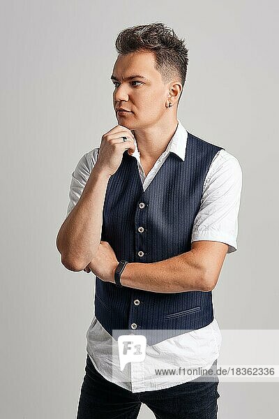 Portrait of trendy man in white shirt and vest posing over gray background
